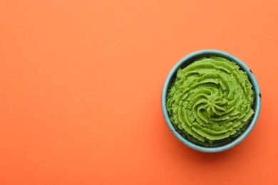 Photo of Bowl with swirl of wasabi paste on orange background, top view. Space for text