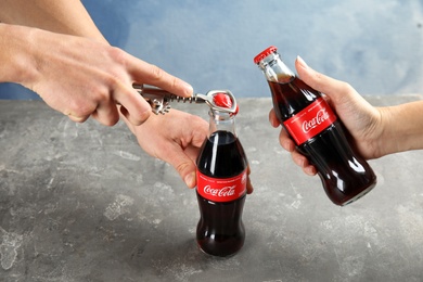 Photo of MYKOLAIV, UKRAINE - NOVEMBER 15, 2018: People with bottles of Coca Cola at table, closeup