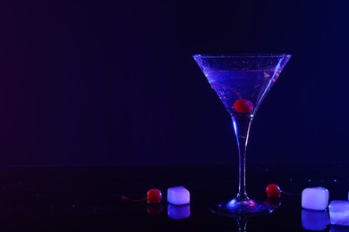 Photo of Fresh martini near ice and cherries on mirror table in neon lights, space for text