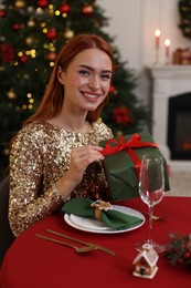 Photo of Beautiful young woman with Christmas gift at served table in room