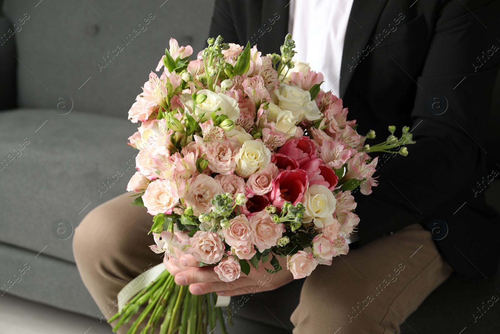 Photo of Man with beautiful bouquet of flowers on sofa indoors, closeup