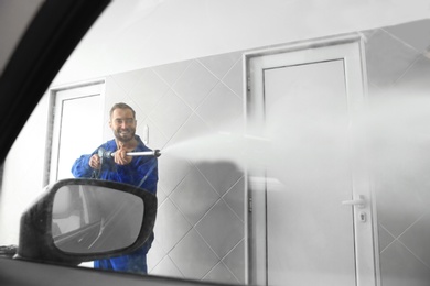 Worker cleaning automobile window with high pressure water jet at car wash, view from inside