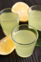 Photo of Tasty limoncello liqueur and lemon on dark wooden table, closeup