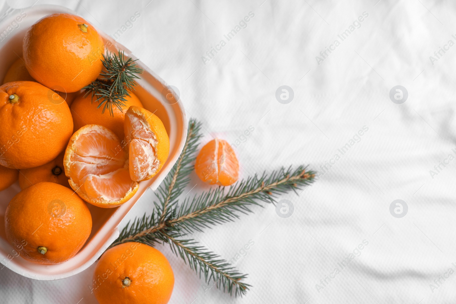 Photo of Box with delicious ripe tangerines and fir branches on white bedsheet, flat lay. Space for text