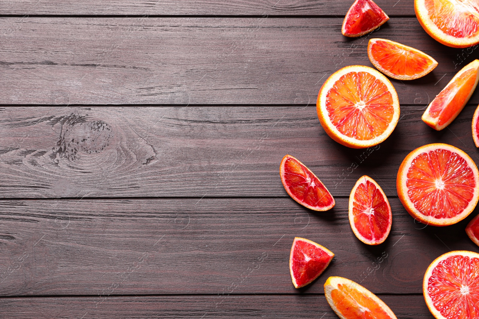 Photo of Cut fresh ripe red oranges on wooden table, flat lay. Space for text