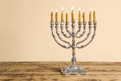 Photo of Silver menorah with burning candles on wooden table against beige background, space for text. Hanukkah celebration