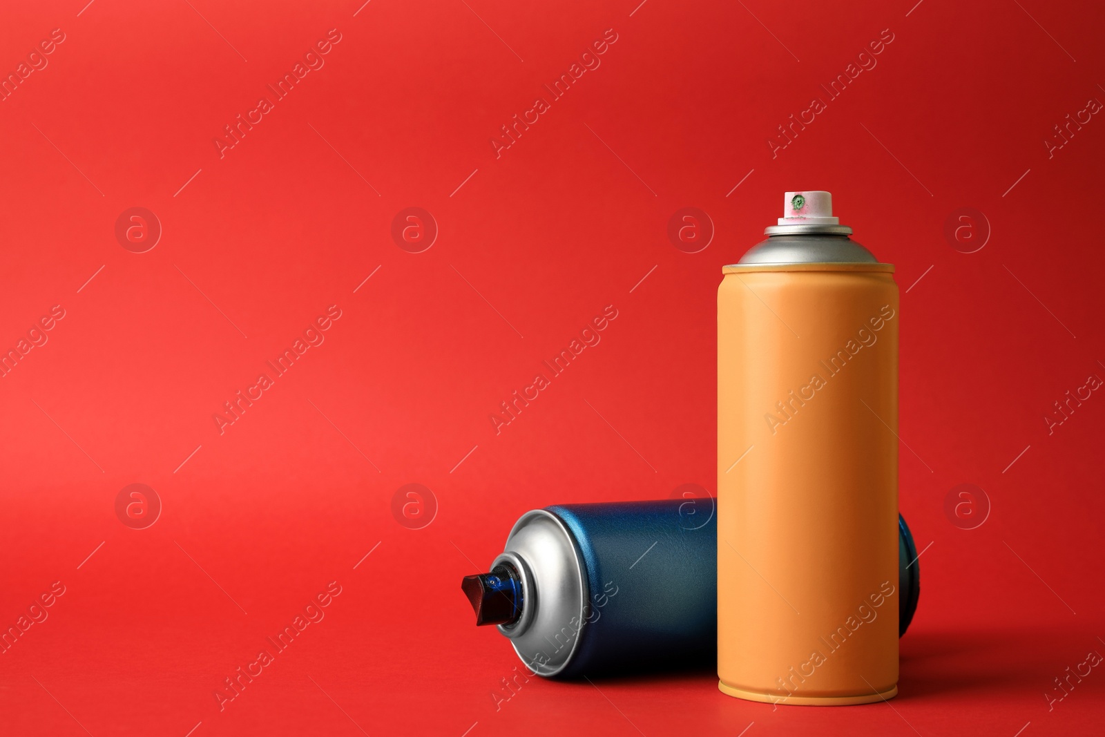 Photo of Cans of different graffiti spray paints on red background, space for text