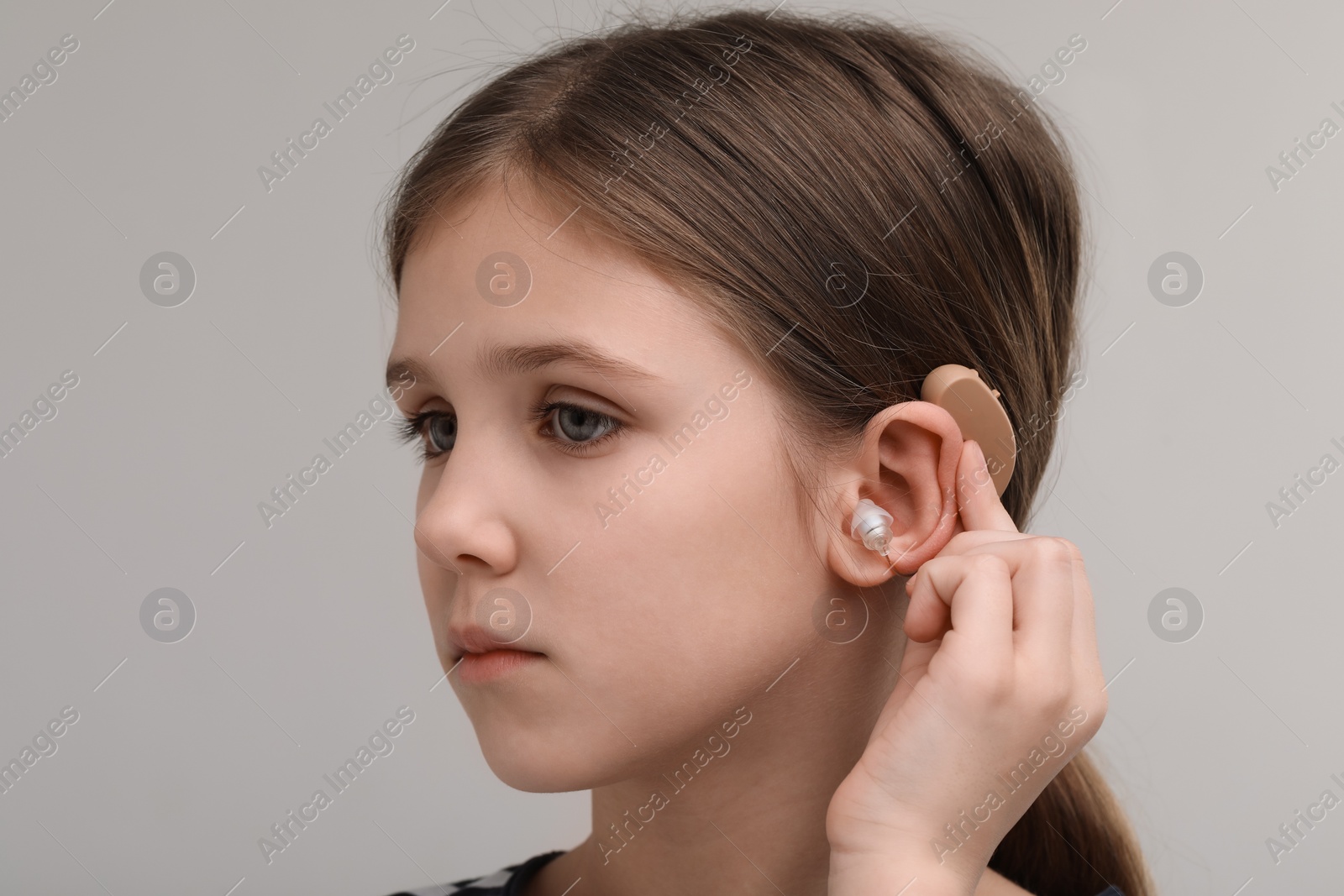 Photo of Little girl with hearing aid on grey background