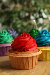Delicious cupcakes with colorful cream on wooden table, closeup
