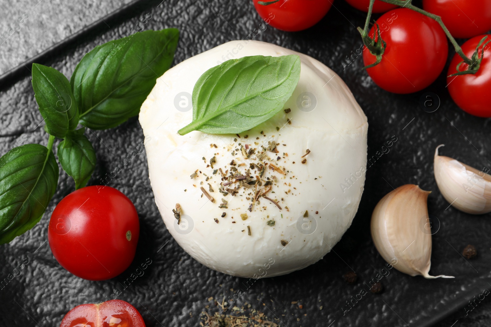 Photo of Delicious mozzarella with tomatoes and basil leaves on black tray, flat lay