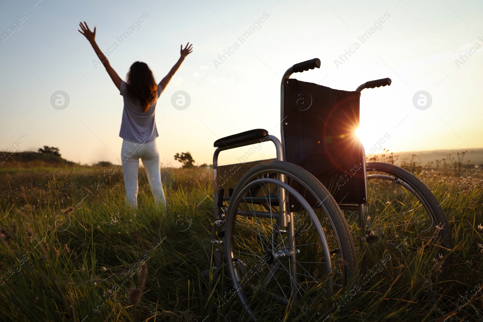 Photo of Woman standing near wheelchair in evening outdoors, back view. Healing miracle