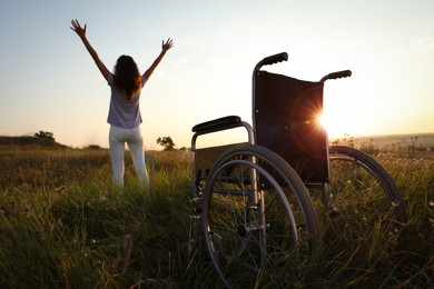 Photo of Woman standing near wheelchair in evening outdoors, back view. Healing miracle