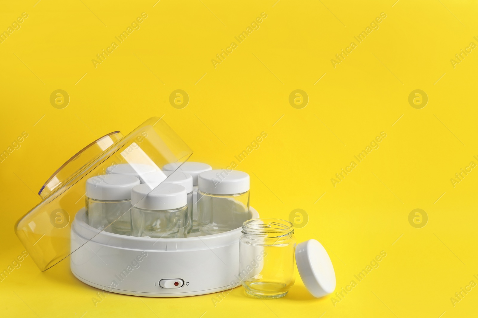 Photo of Modern yogurt maker with empty jars on yellow background, space for text