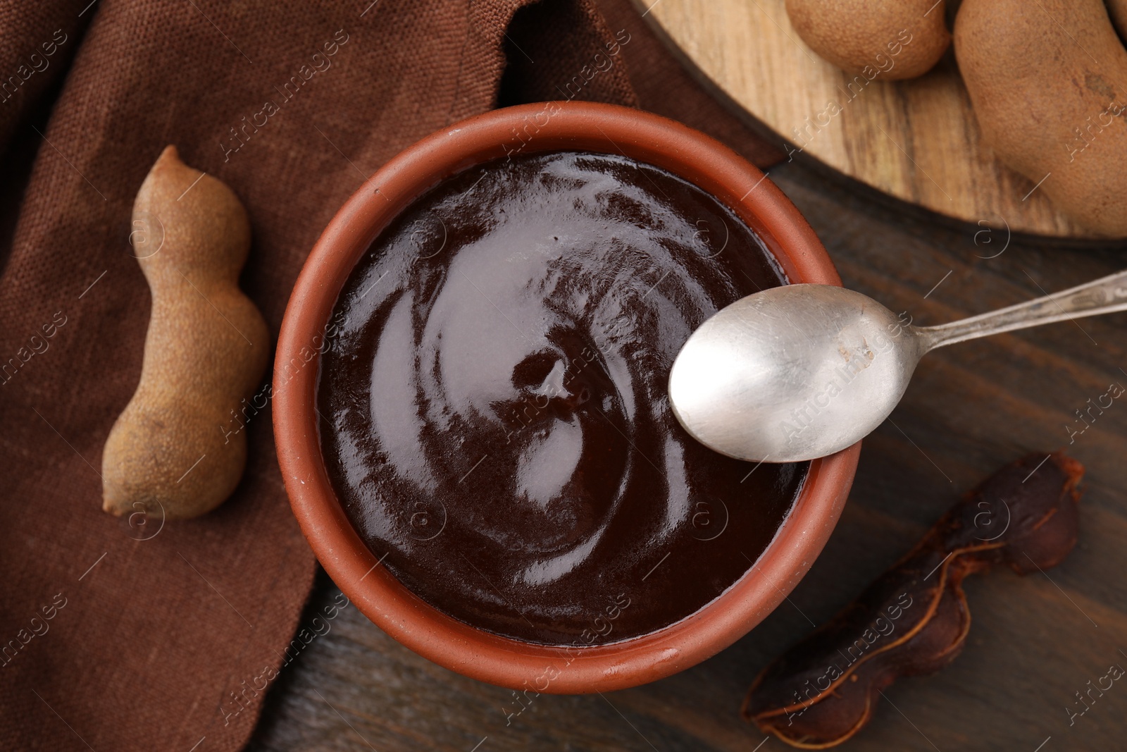 Bowl of tamarind sauce, spoon and fresh pods on wooden table, flat lay Photo of Bowl of tamarind sauce, spoon and fresh pods on wooden table, flat lay