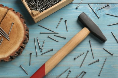 Photo of Hammer, crate and metal nails on light blue wooden table, flat lay