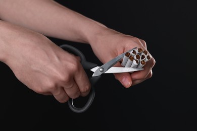 Photo of Stop smoking concept. Woman cutting cigarettes on black background, closeup