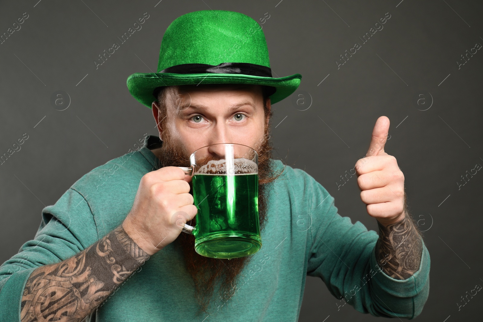 Photo of Bearded man drinking green beer on grey background. St. Patrick's Day celebration