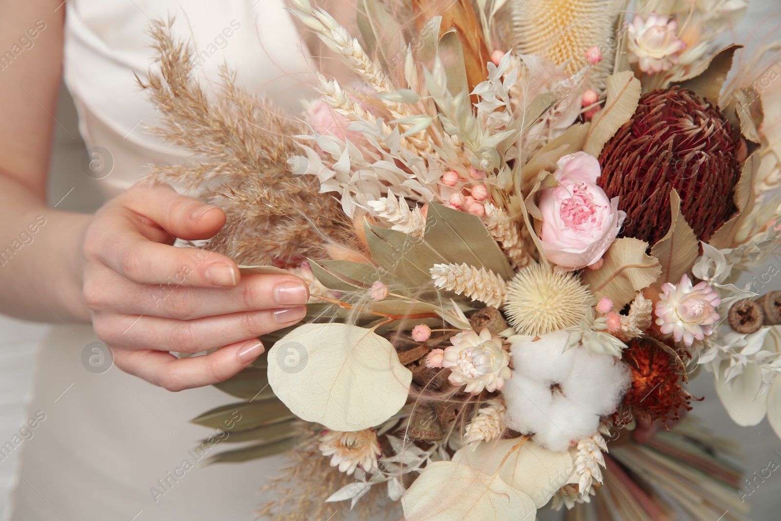 Photo of Bride holding beautiful dried flower bouquet indoors, closeup