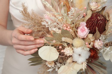 Bride holding beautiful dried flower bouquet indoors, closeup