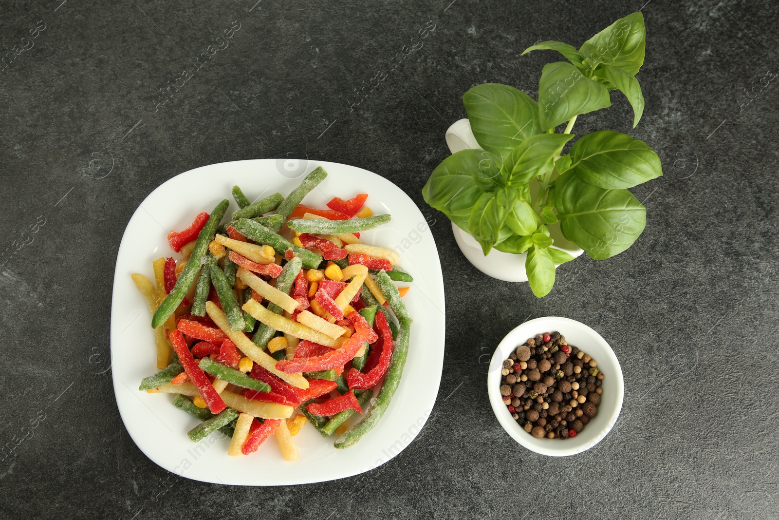 Photo of Mix of different frozen vegetables, basil and spices on gray table, flat lay