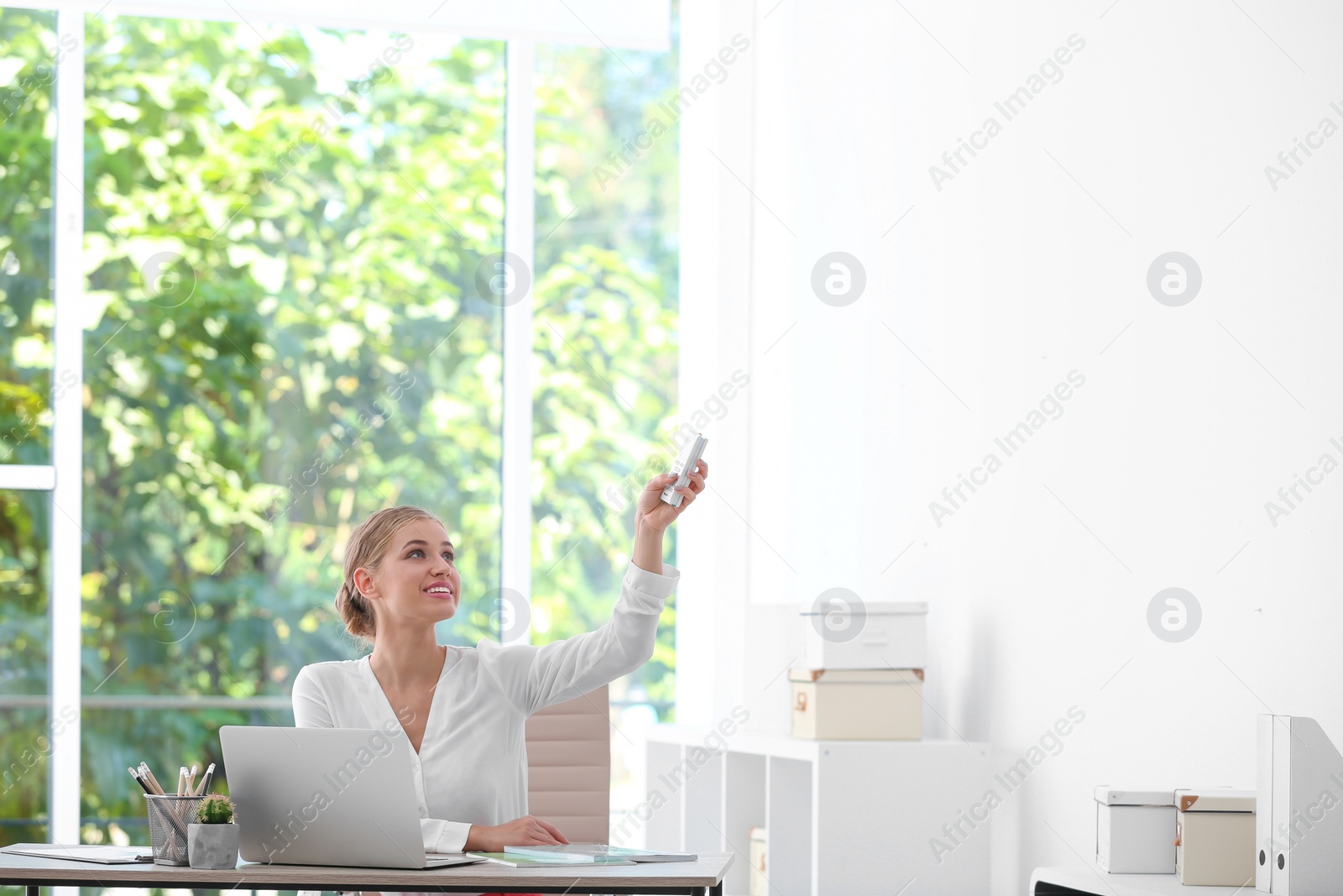 Photo of Young woman with air conditioner remote in office