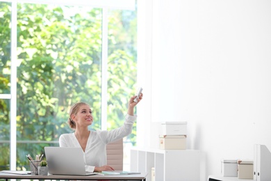 Photo of Young woman with air conditioner remote in office