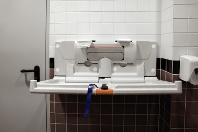 Photo of Modern baby changing table on tiled wall in public toilet