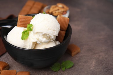 Tasty ice cream with caramel candies and mint in bowl on brown table, closeup. Space for text