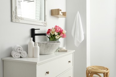 Vase with beautiful pink tulips and toiletries near sink in bathroom