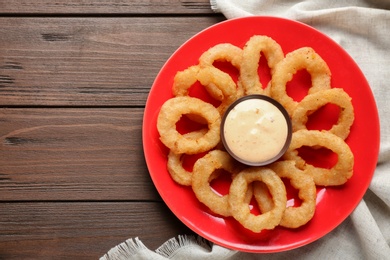 Photo of Plate with fried onion rings and sauce on table, top view