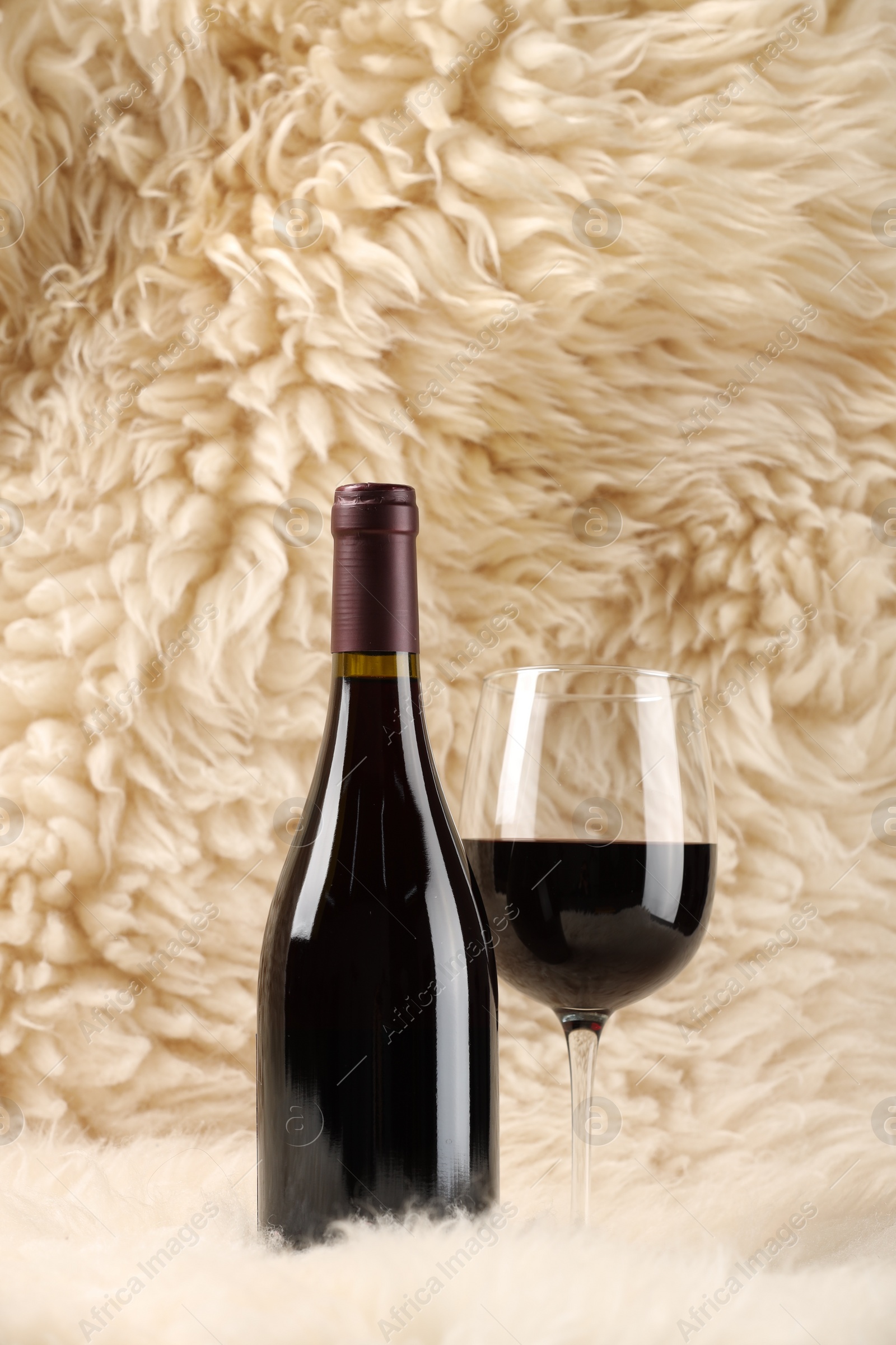 Photo of Stylish presentation of delicious red wine in bottle and glass on fluffy surface