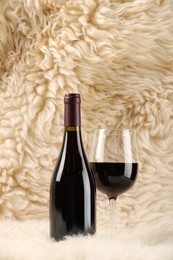 Stylish presentation of delicious red wine in bottle and glass on fluffy surface