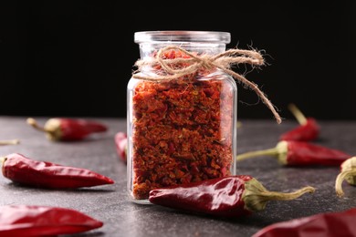 Photo of Chili pepper flakes in jar and pods on textured table against black background, closeup