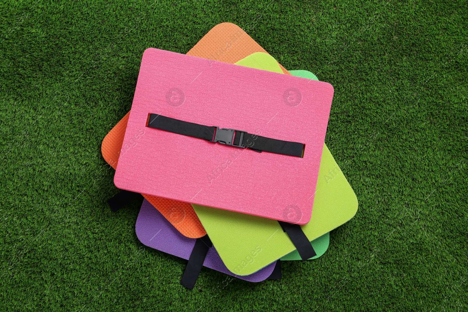 Photo of Bright foam tourist seat mats on green grass, flat lay