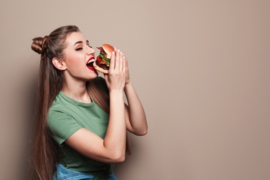 Pretty woman eating tasty burger on color background. Space for text