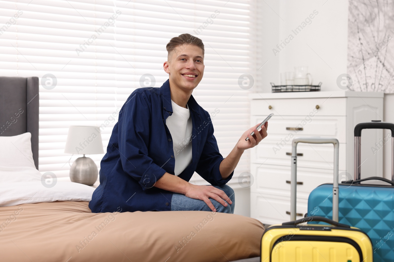 Photo of Smiling guest with smartphone on bed in stylish hotel room