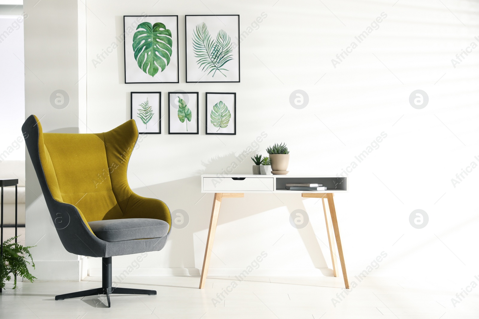 Photo of Stylish room interior with comfortable armchair and paintings of tropical leaves