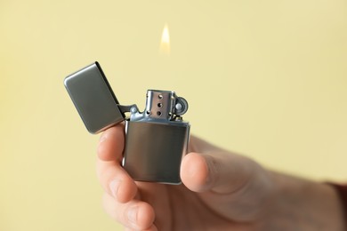 Photo of Man holding lighter with burning flame against beige background, closeup