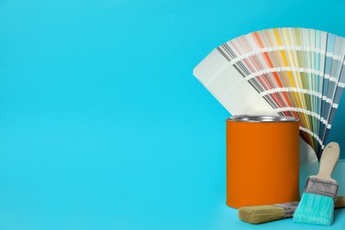 Can of orange paint, color palette samples and brushes on turquoise background. Space for text