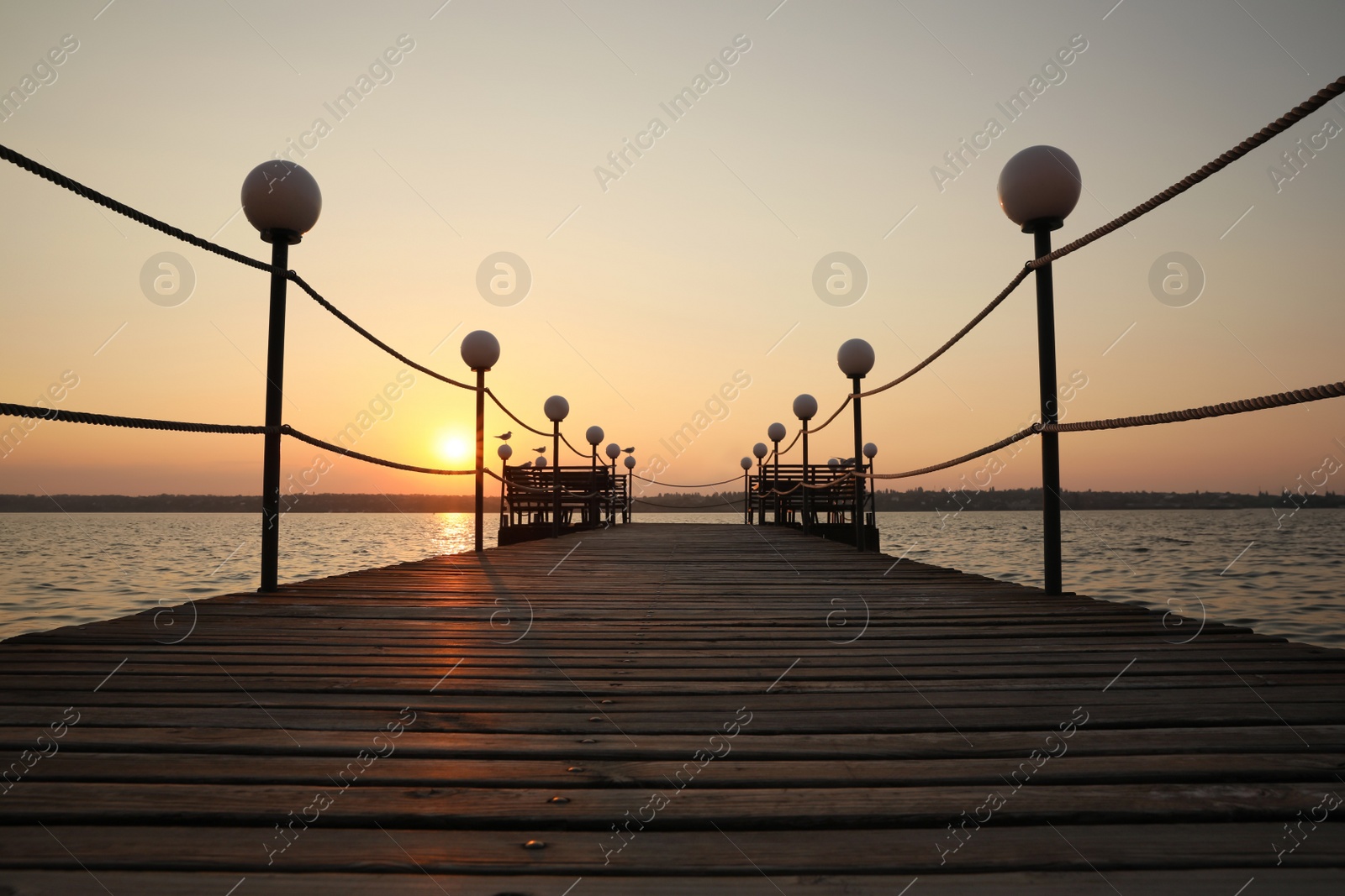 Photo of Picturesque view of empty wooden pier with lanterns at sunset