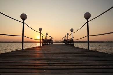 Photo of Picturesque view of empty wooden pier with lanterns at sunset