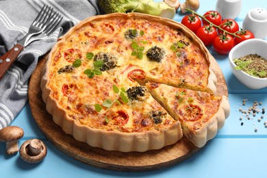 Photo of Delicious homemade vegetable quiche and ingredients on light blue wooden table