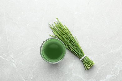Photo of Glass of wheat grass juice and green sprouts on grey marble table, flat lay