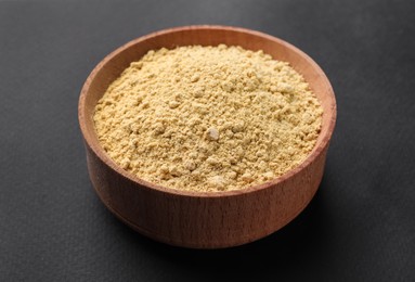 Photo of Aromatic mustard powder in wooden bowl on dark background