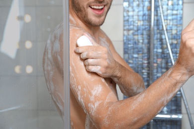 Photo of Young man taking shower with soap in bathroom, closeup