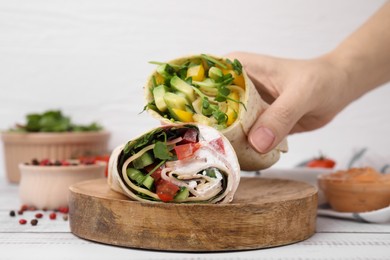 Woman holding delicious sandwich wraps with fresh vegetables at white wooden table, closeup