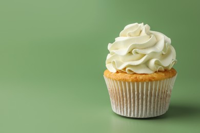 Photo of Tasty vanilla cupcake with cream on green background, closeup. Space for text