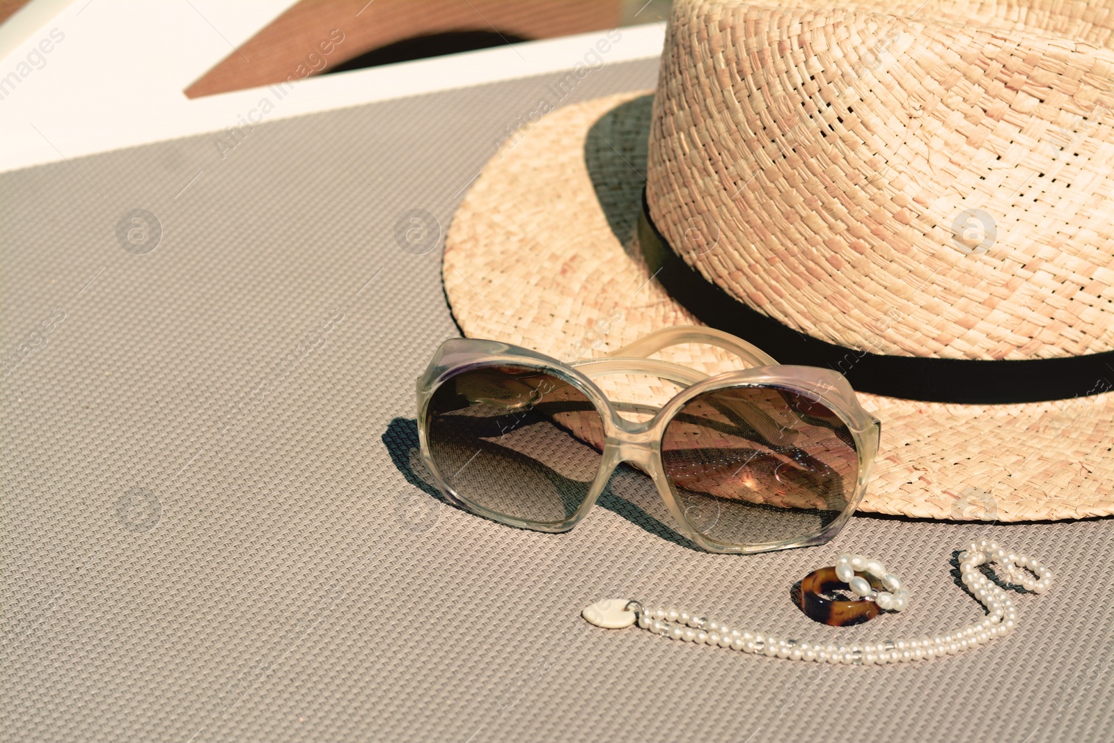 Photo of Stylish hat, sunglasses and jewelry on grey sunbed outdoors, space for text