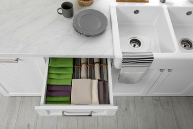 Photo of Open drawer with different folded towels and napkins in kitchen, above view