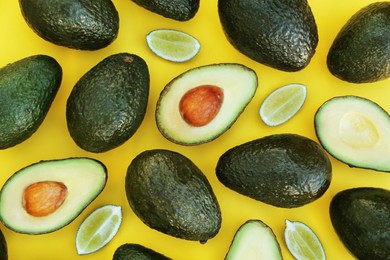 Photo of Many fresh whole and cut avocados with limes on yellow background, flat lay